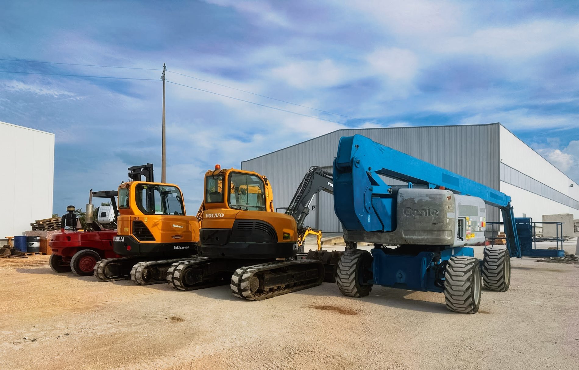 Plataforma elevatória Genie azul e escavadoras Volvo e Hyundai alinhadas no parque exterior da Primeheavy