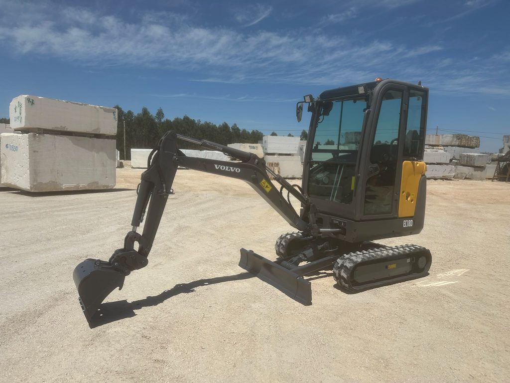Mini-escavadora Volvo EC18D de perfil com o braço mecânico e balde estendidos sobre o terreno