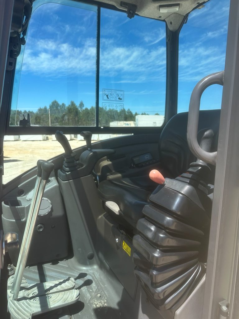 Interior da cabine da mini-escavadora Volvo com foco nos manípulos de controlo, joysticks e pedais