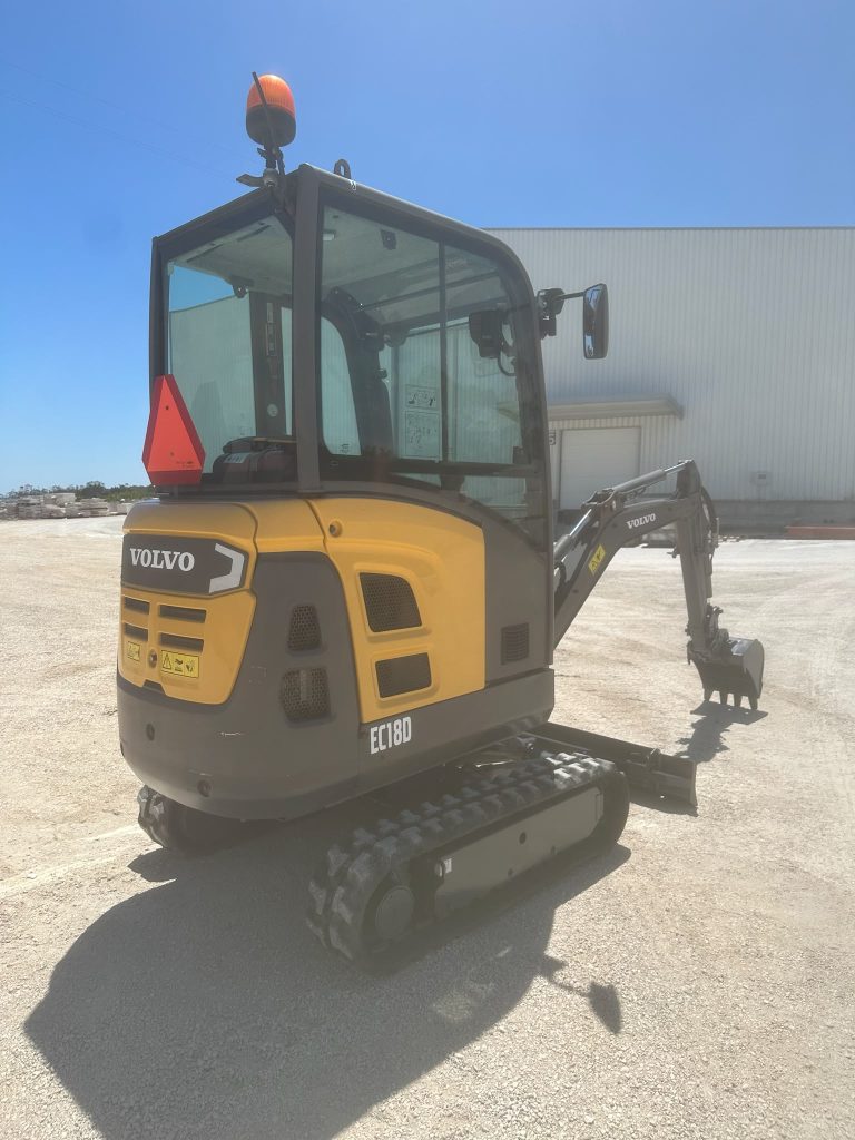 Parte traseira da mini-escavadora Volvo EC18D destacando o capô do motor e o triângulo de sinalização